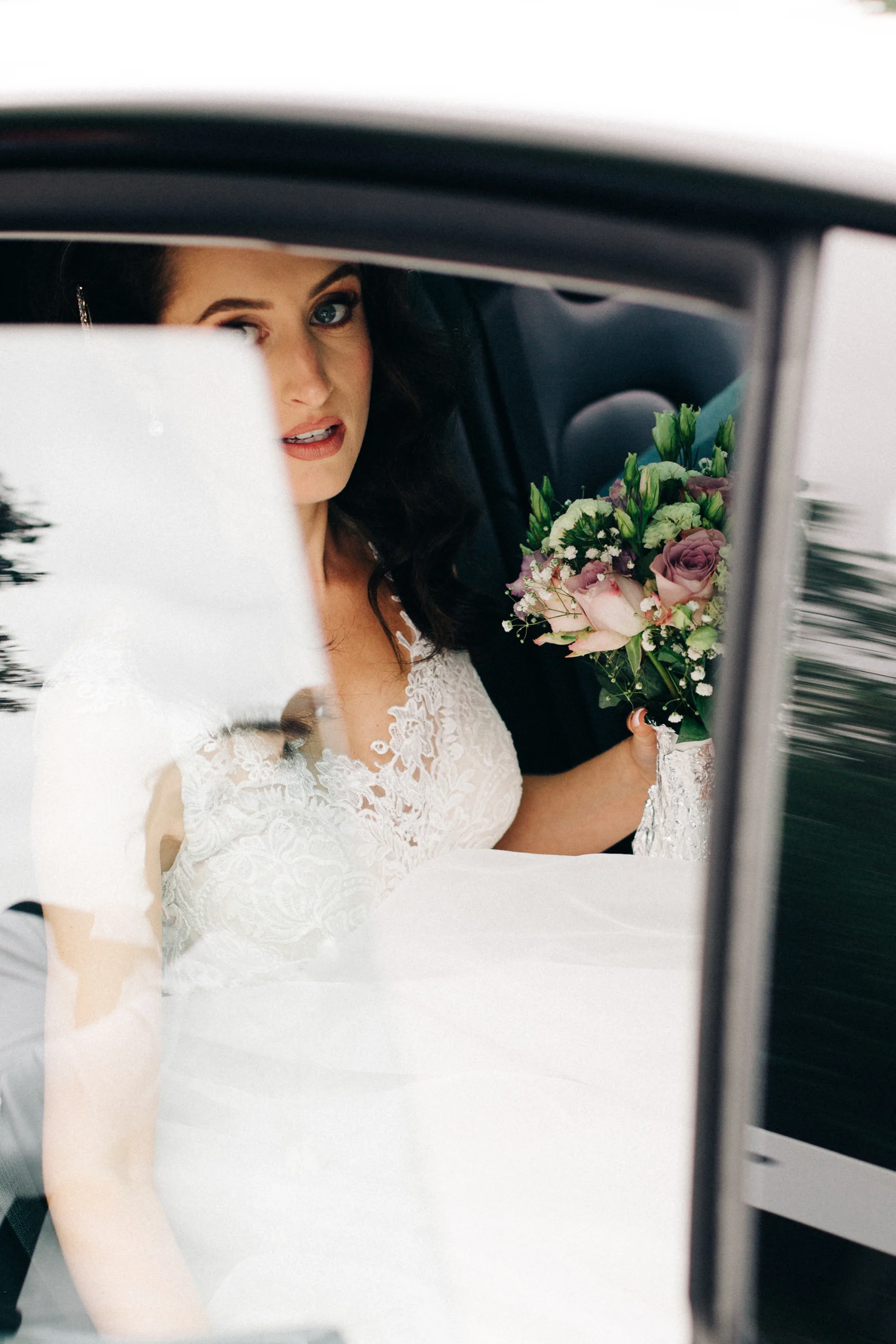Mariée au bouquet de fleurs vue à travers la vitre de la voiture