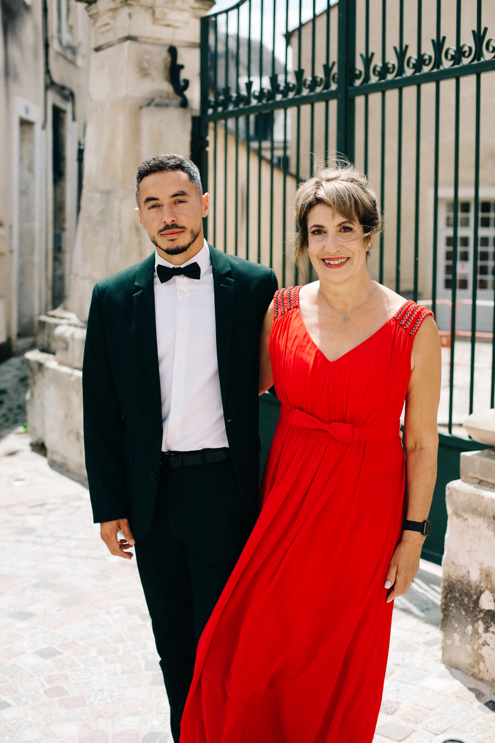 Invités élégants, costume noir et robe rouge, dans une ruelle pavée de Bourges