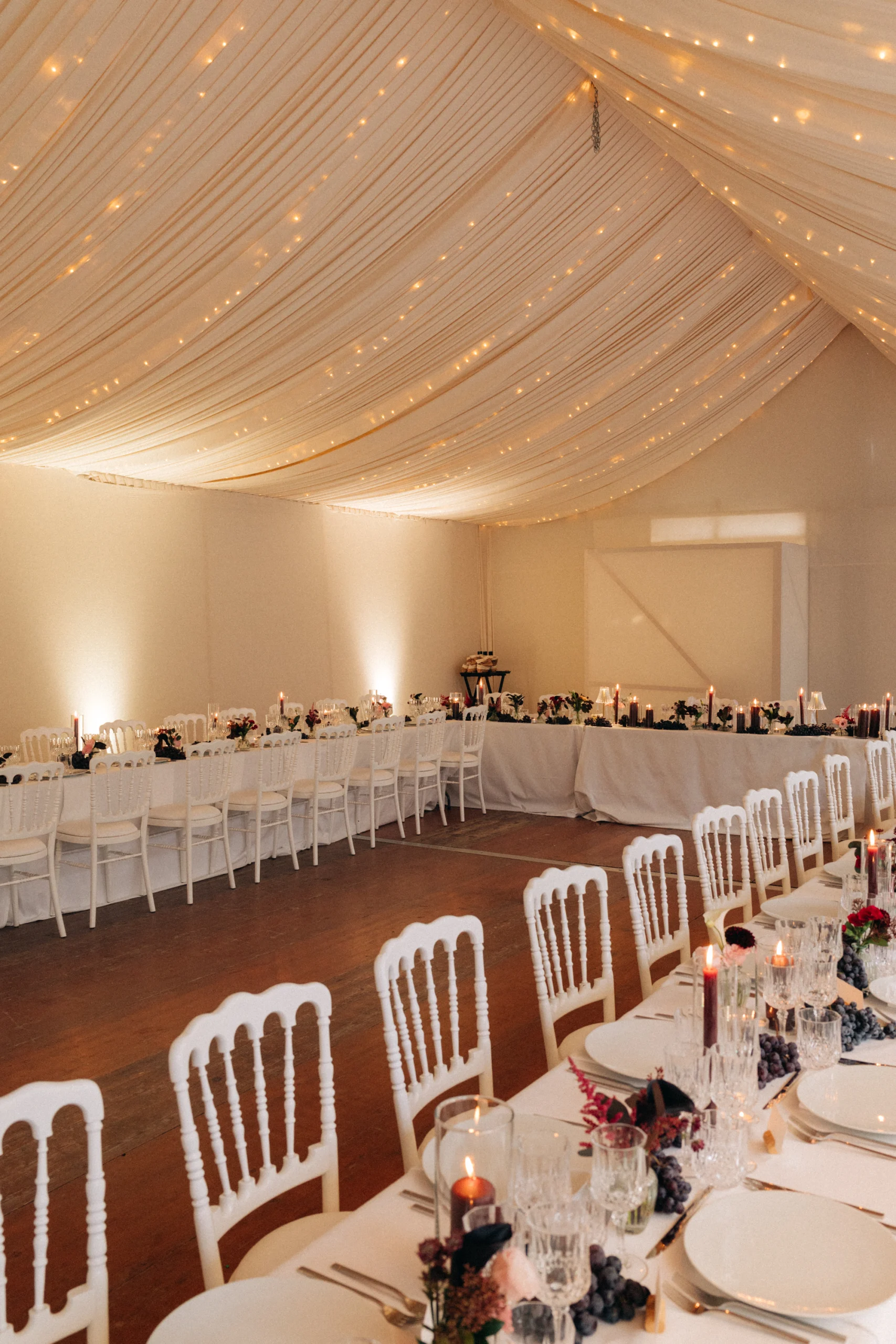 Salle de réception sous chapiteau drapé et guirlandes lumineuses, mariage au Château de Thorens
