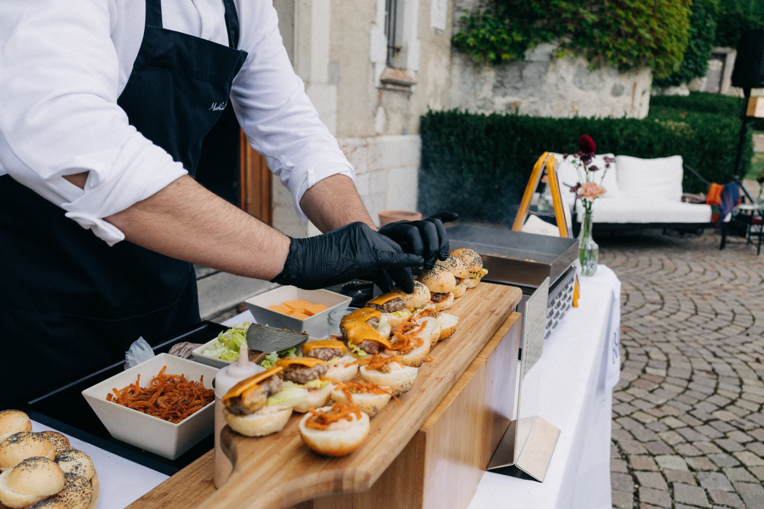 Traiteur dressant des mini-burgers sur une planche en bois pendant le cocktail