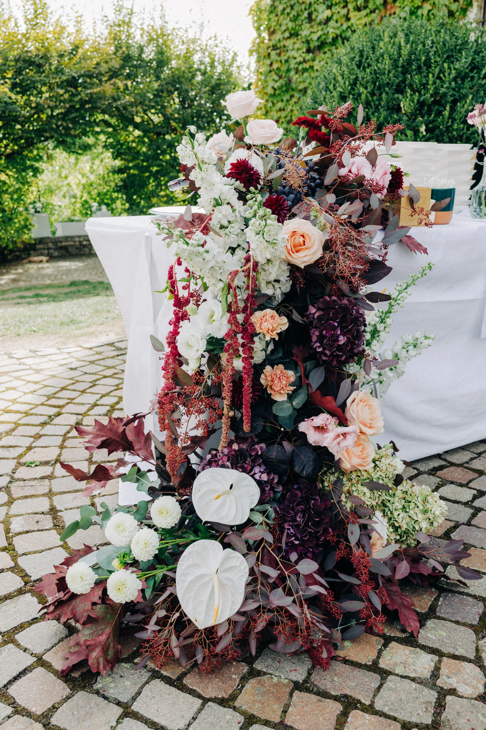 Composition florale aux roses, anthuriums et feuillages bordeaux par le fleuriste