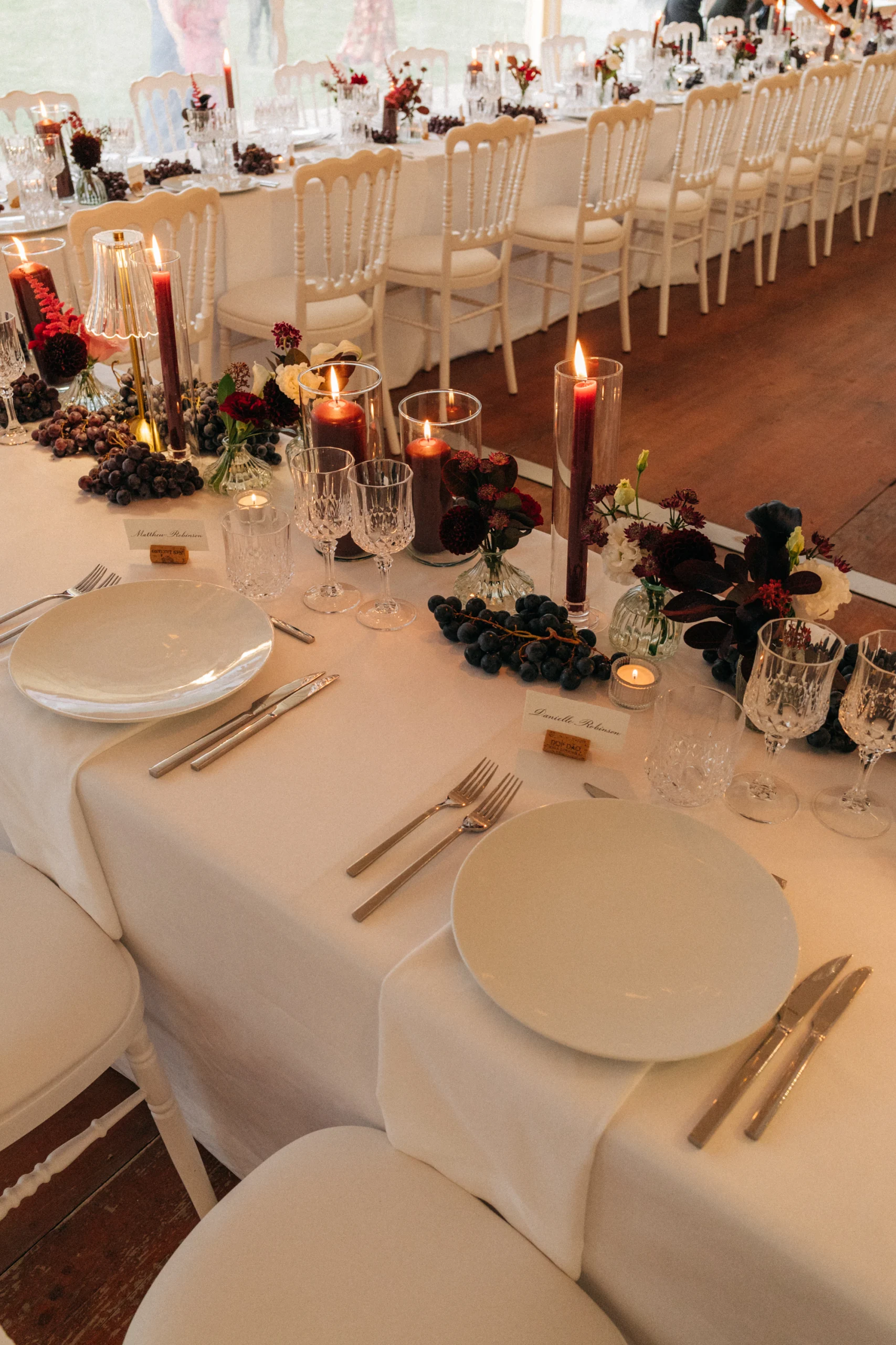 Table de mariage dressée : bougies bordeaux, raisins et fleurs sur nappe blanche