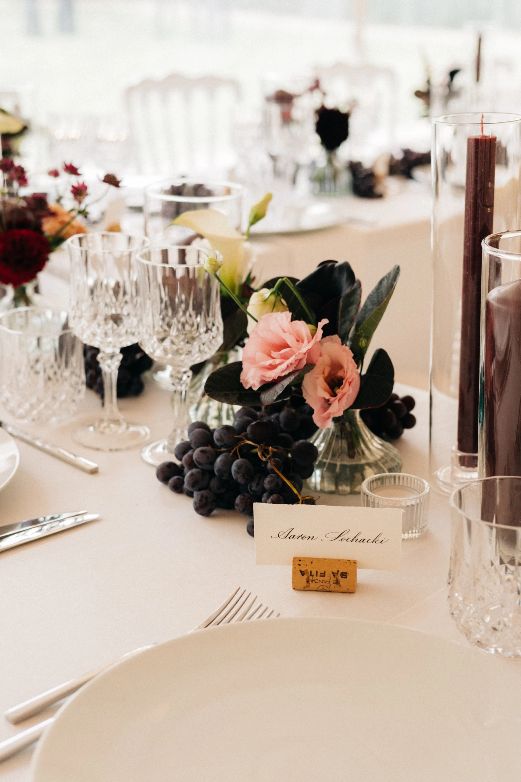 Détail de table : marque-place, verres en cristal et bouquet de roses et raisins
