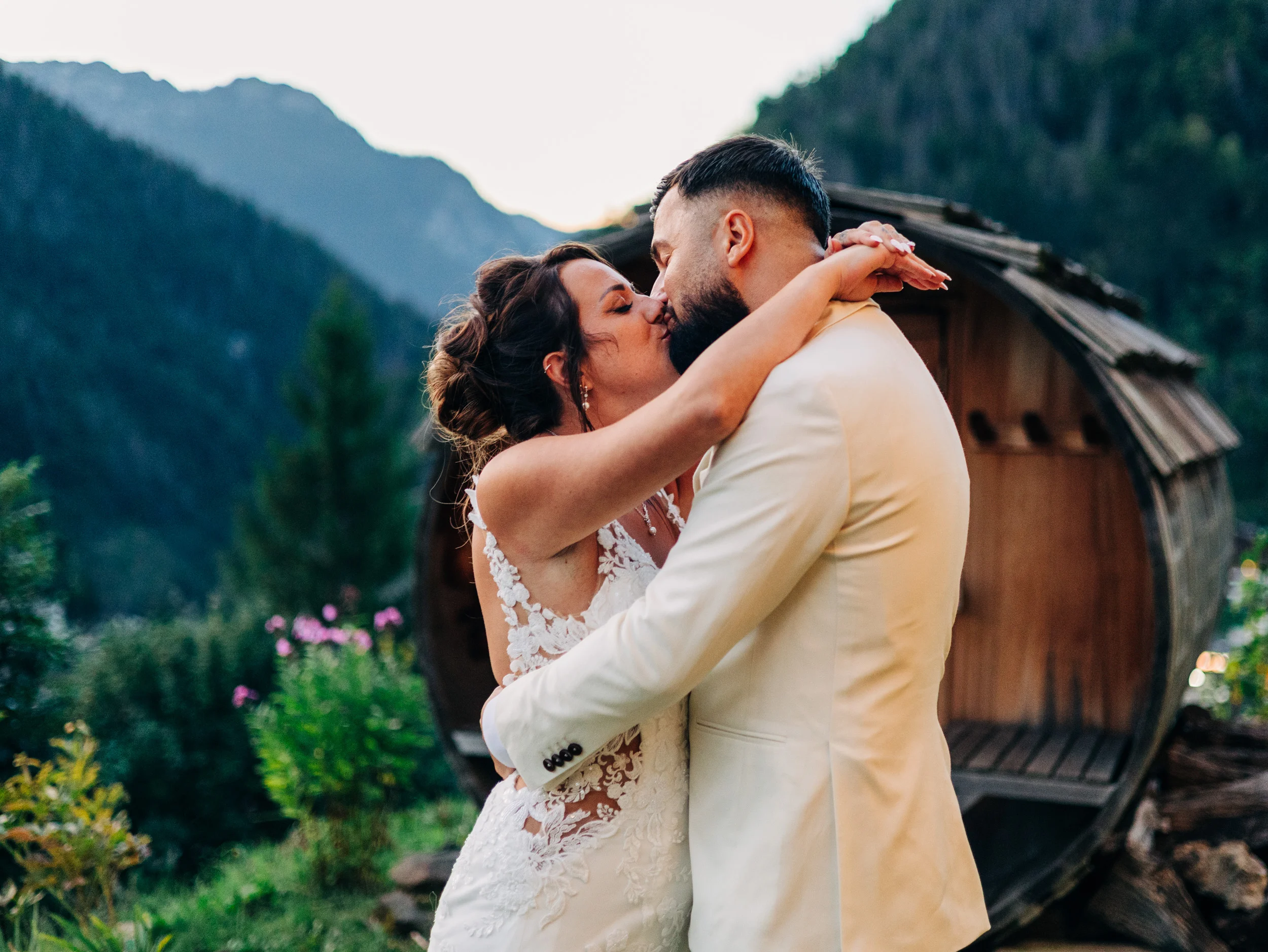 Mariés s'embrassant devant un grand tonneau en bois, montagnes des Aravis en arrière-plan, mariage à La Clusaz