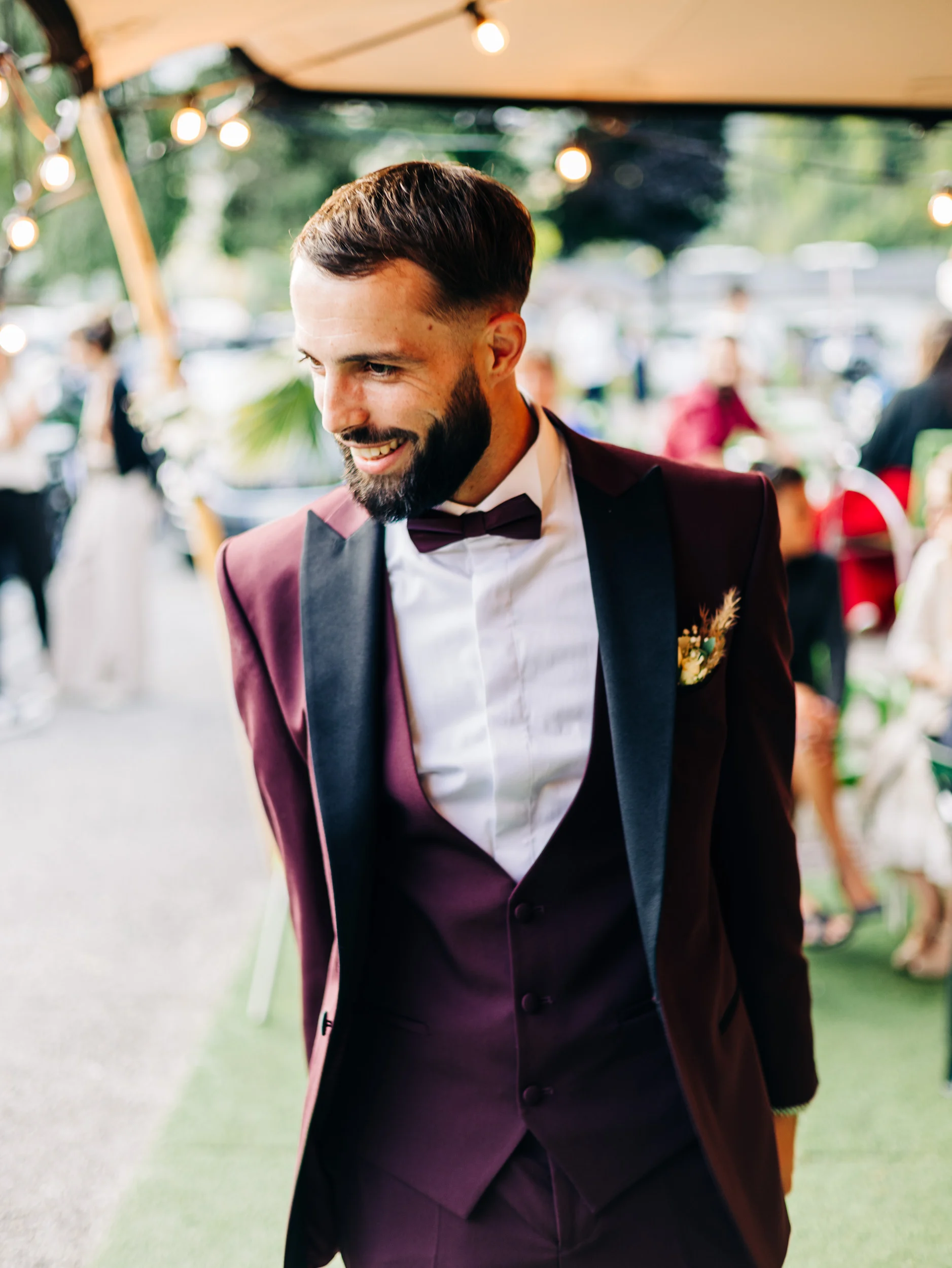 Témoin en costume bordeaux et nœud papillon souriant pendant le cocktail