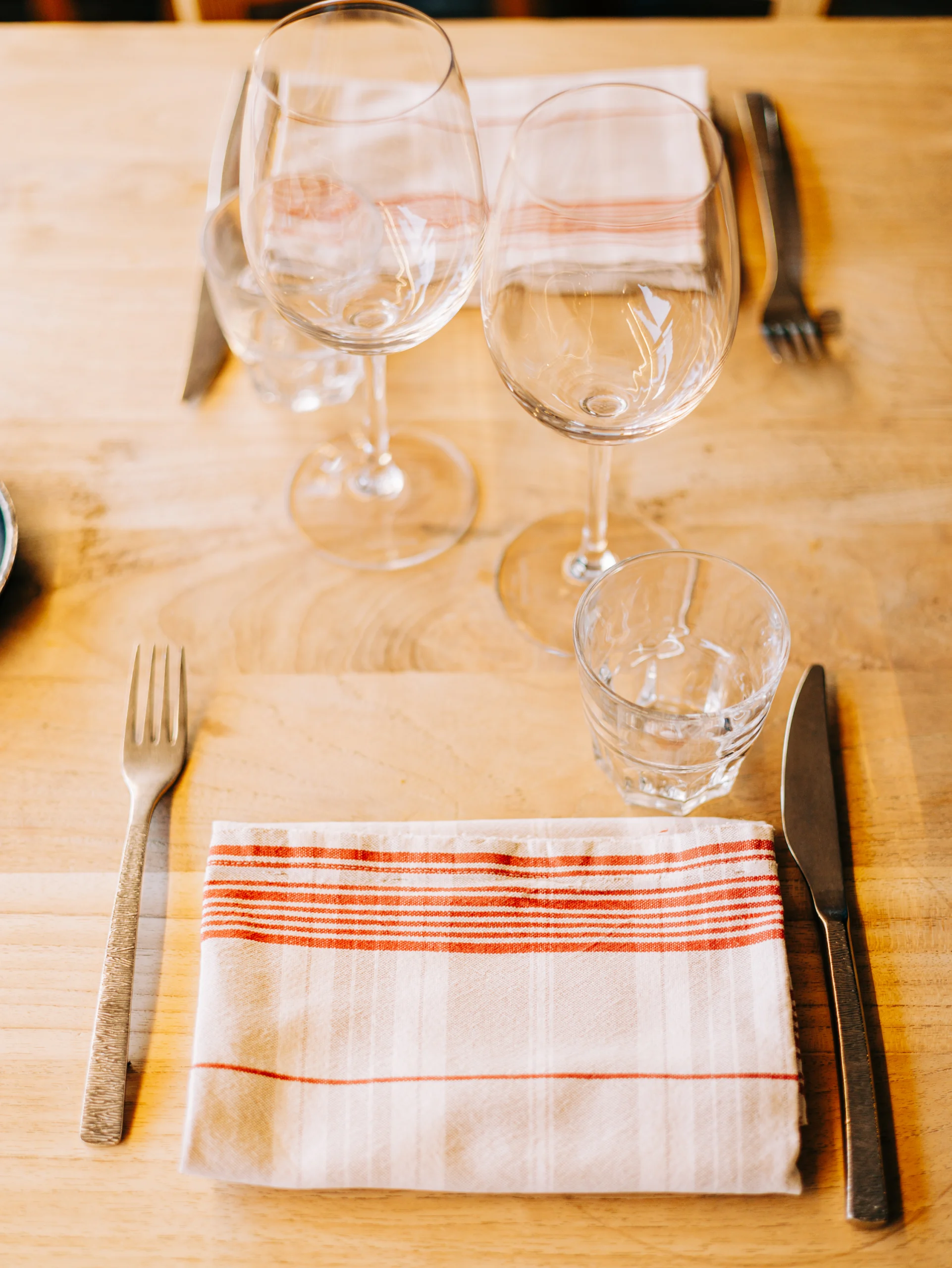 Détail de la table de mariage : verres, couverts et serviette rayée rouge sur bois brut