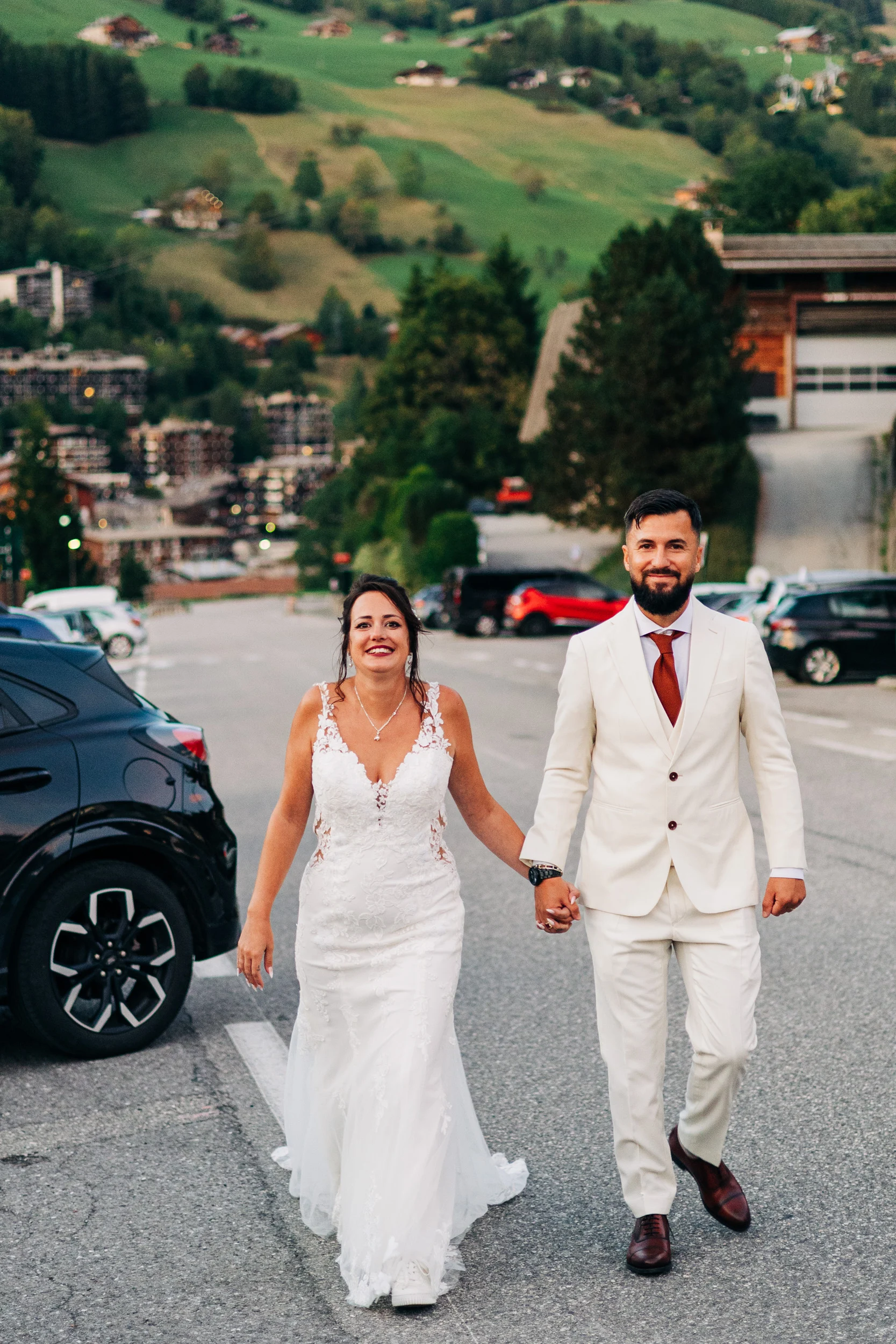 Mariés marchant main dans la main dans les rues de La Clusaz, montagnes en arrière-plan