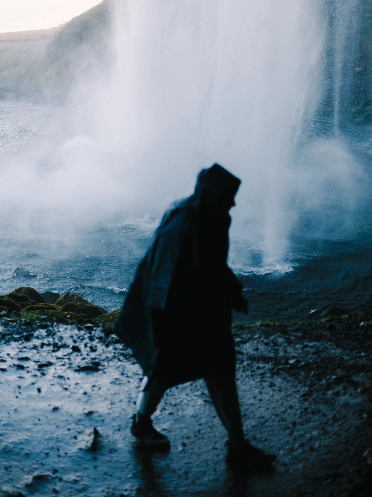 Silhouette en cape de pluie derrière la cascade de Seljalandsfoss