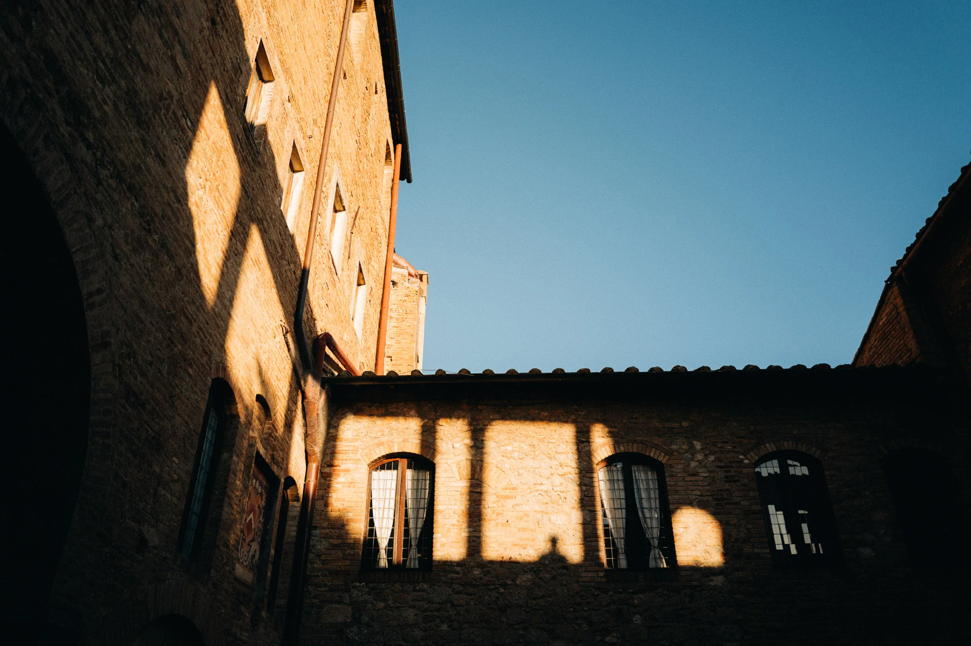 Lumière rasante sur les façades en briques d'une cour médiévale en Toscane