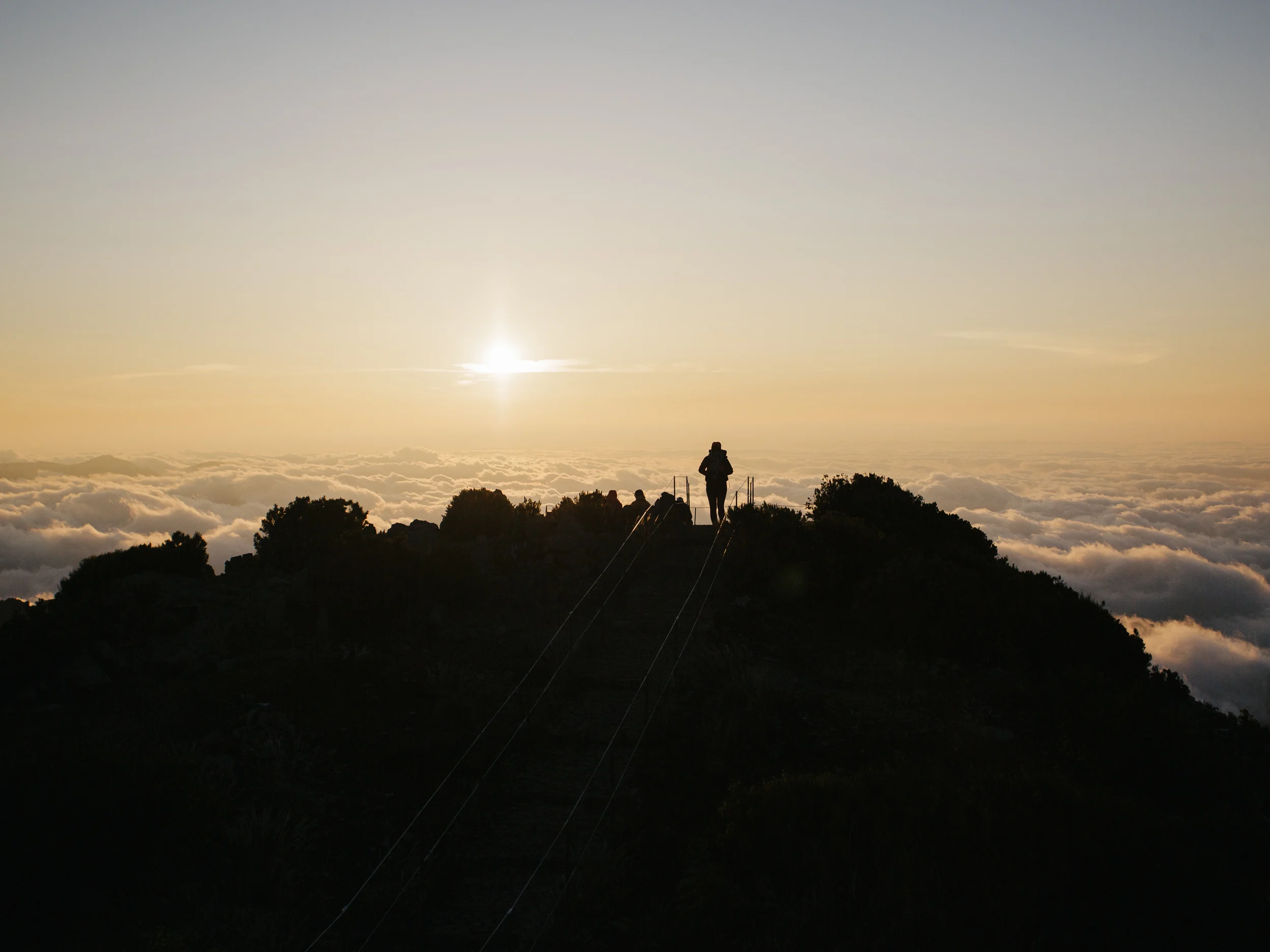 Silhouette d'un randonneur face au soleil levant au-dessus des nuages