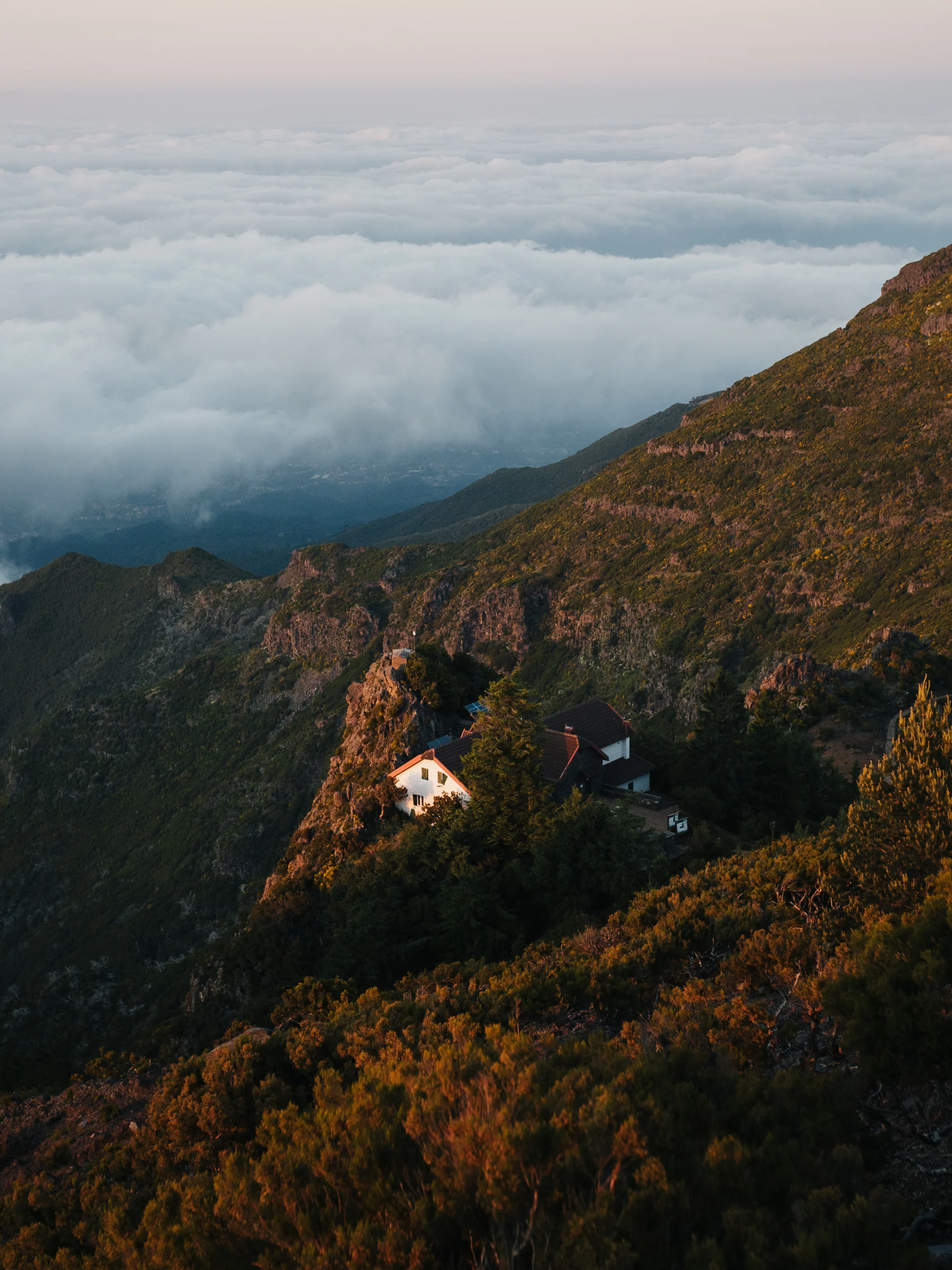 Maison isolée sur un versant de montagne au-dessus d'une mer de nuages