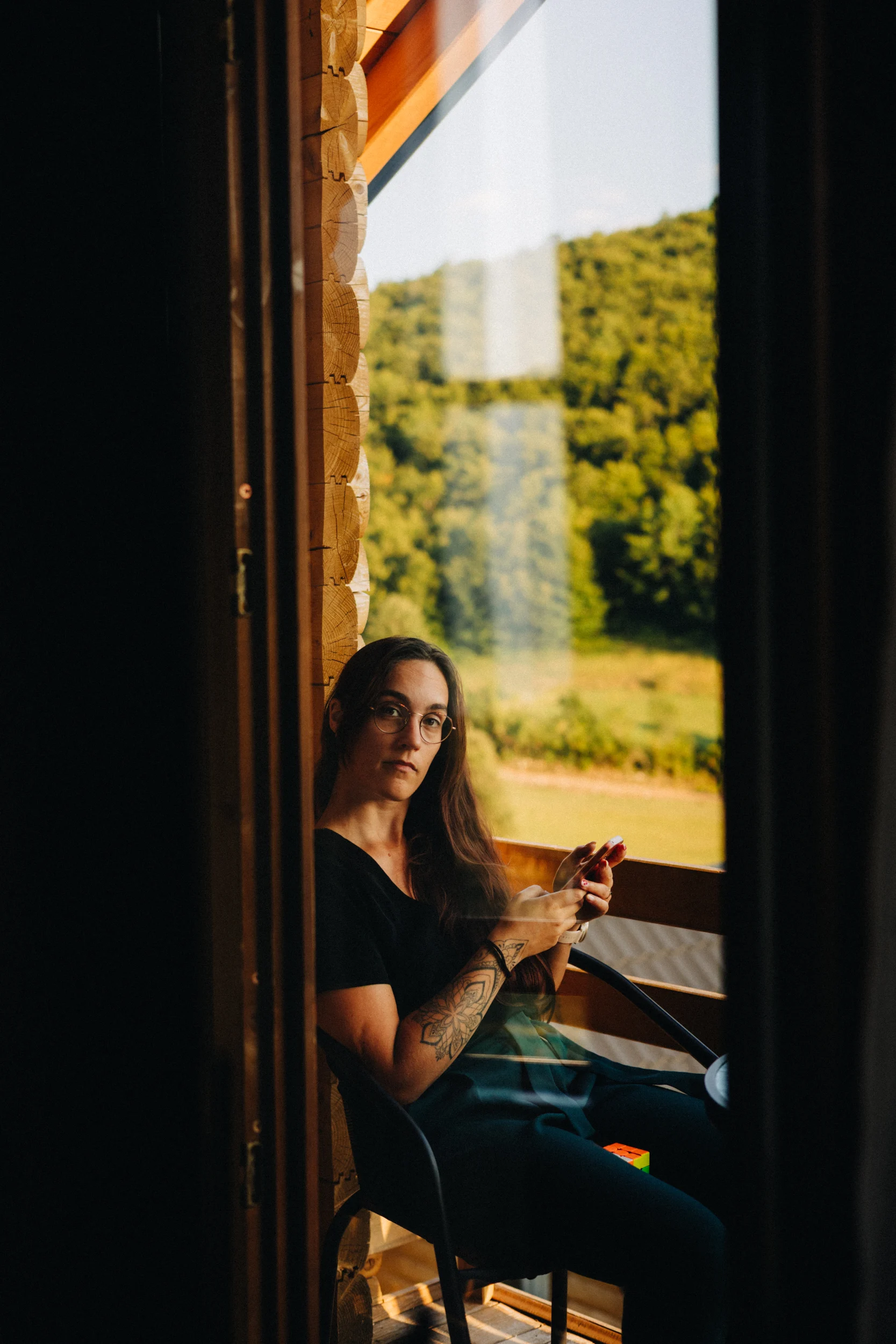Femme assise à la fenêtre d'un chalet en bois, regard vers l'objectif